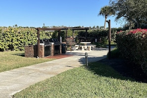 Zona de barbacoa al aire libre con parrilla, asientos y un sendero.
