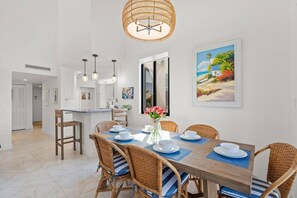 A dining area with a wooden table, wicker chairs, and a hanging light fixture. - Top-Floor Sky Loft at Excelsior: 22’ Ceilings | Private Beach | Pool Views | Pro Remote Work Setup (Sarasota)