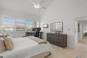 Ein Schlafzimmer mit Bett, Schreibtisch, Stuhl, Kommode und Deckenventilator.