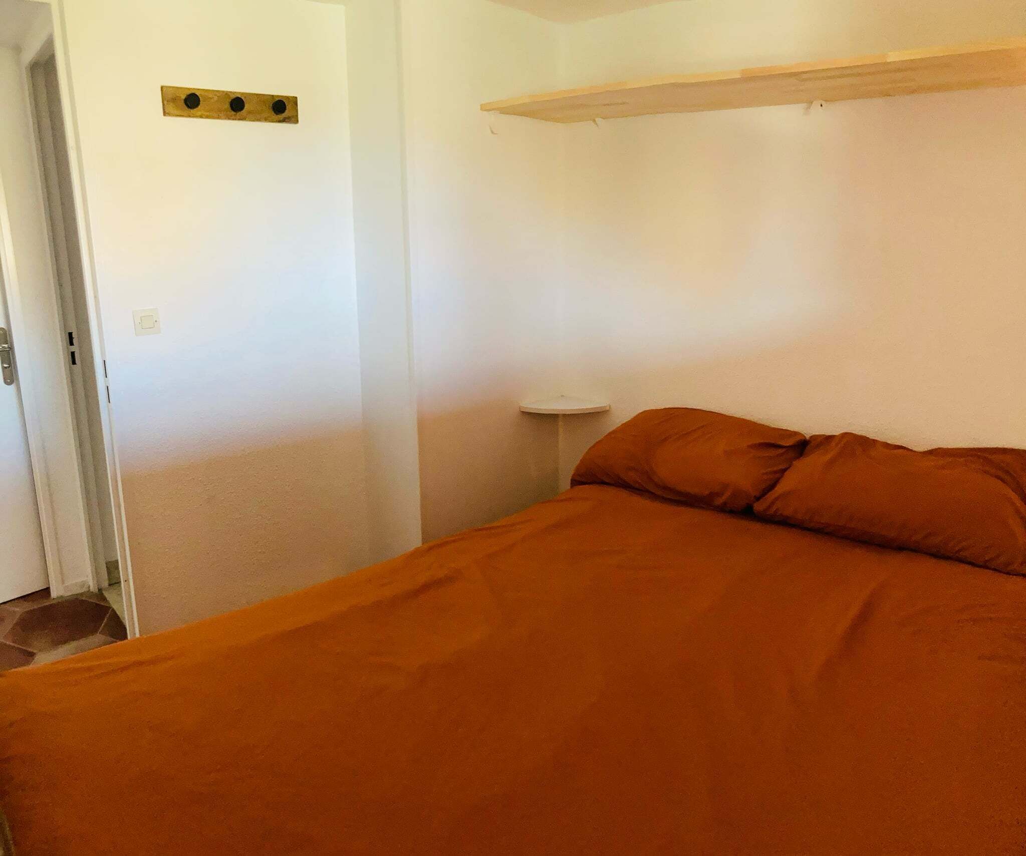 Une chambre à coucher avec un lit, une table de chevet et une étagère fixée au mur.