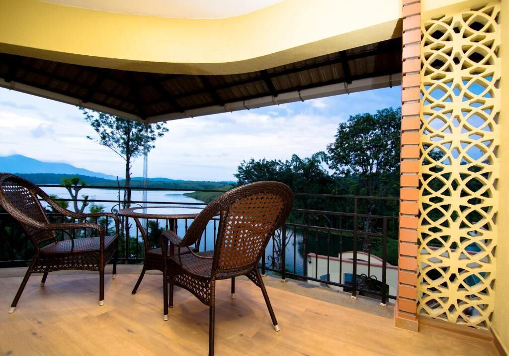 A balcony with wicker chairs and a table, overlooking a body of water and distant mountains.