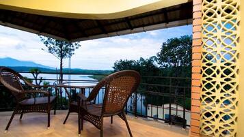 A balcony with wicker chairs and a table, overlooking a body of water and distant mountains.