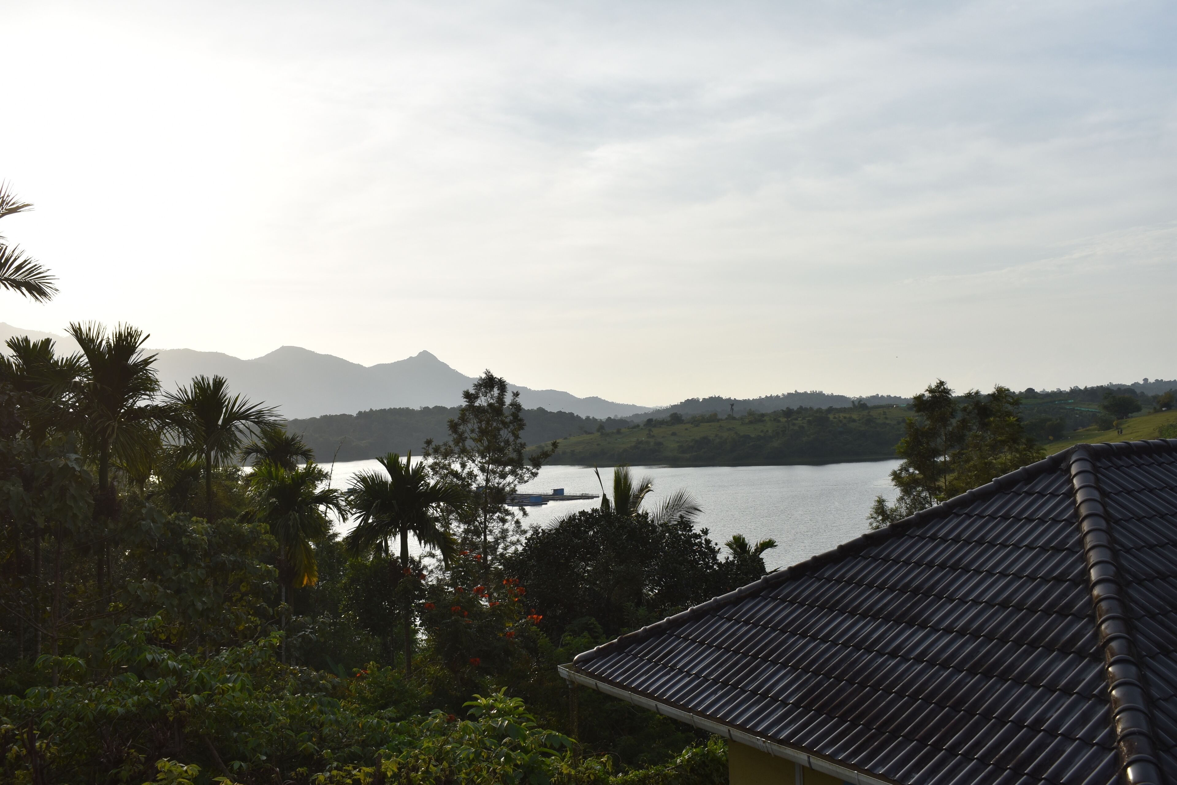 A view of a lake with mountains in the background, surrounded by greenery and a building with a tiled roof.