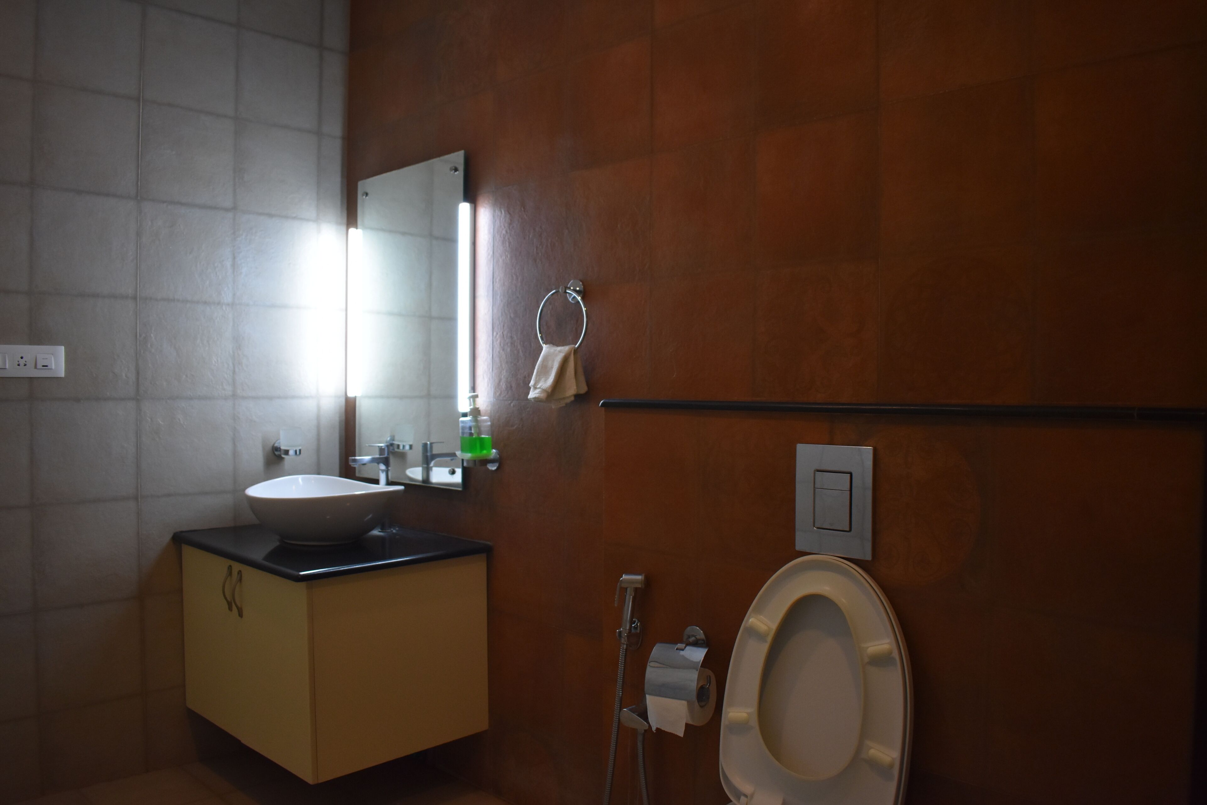 A bathroom with a sink, mirror, towel ring, toilet, and a showerhead.