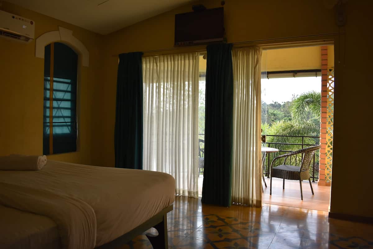 Habitación de hotel con cama, ventana con cortinas y puerta que da a un espacio exterior con una silla y una mesa.