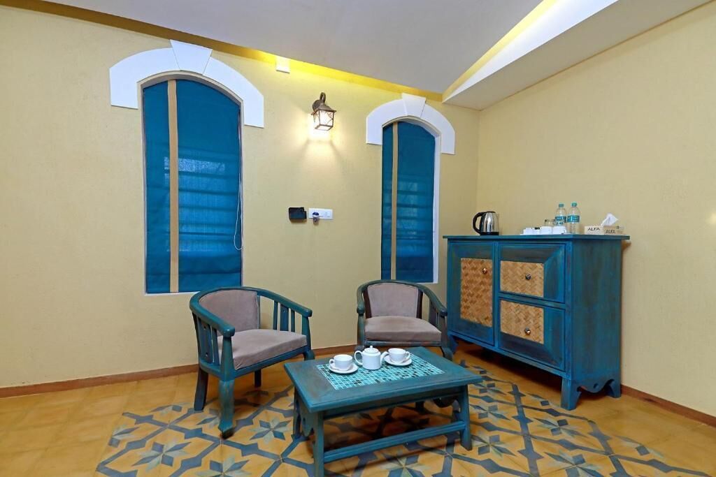 A room with two chairs, a table with teapots, a cabinet with water bottles, and a patterned floor.