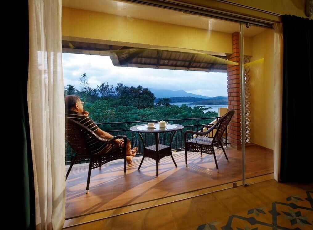 A balcony with wicker chairs and a small table, overlooking a scenic view of a lake and mountains.