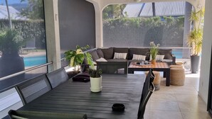 Un espace repas extérieur moderne avec vue sur la piscine, doté d’un ventilateur de plafond et d’un mobilier confortable.
