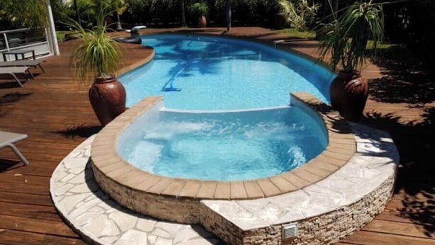 Une piscine avec un jacuzzi, entourée d’une terrasse en bois et de plantes en pot.