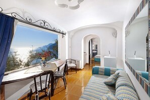 Ein Zimmer mit großem Fenster, einer Couch, einem Esstisch und einem Stuhl.
