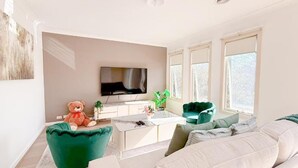 A modern living room with a flat-screen TV, green armchairs, a sofa, and a marble coffee table. - StayAU Family Haven Pet-Friendly (Caroline Springs)