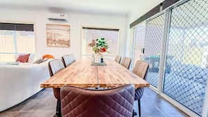 A dining area with a wooden table and chairs, a vase with flowers, and a sliding glass door to the outside. - StayAU Family Haven Pet-Friendly (Caroline Springs)