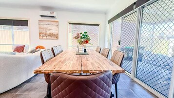Un comedor con mesa y sillas de madera, un jarrón con flores, y un ventanal corredizo al exterior.