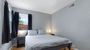 A bedroom with a bed, nightstands, a lamp, a window with curtains, and a radiator. - Spacious Family Home with Game Room, 3 Beds 2 Bath (Elgin)