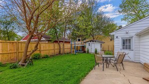 A backyard with a wooden fence, a small shed, and a patio area with chairs and a table. - Spacious Family Home with Game Room, 3 Beds 2 Bath (Elgin)