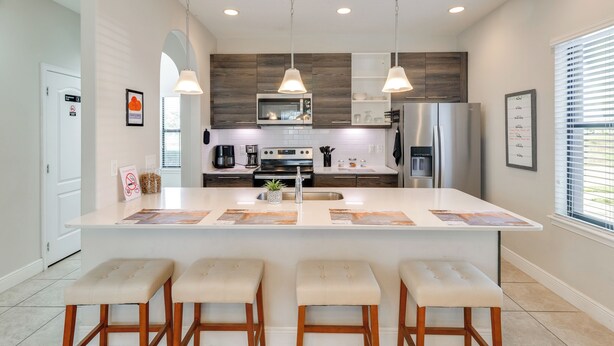 A modern kitchen with a central island, bar stools, pendant lighting, and stainless steel appliances. - Golf, Dine & Unwind Poolside! Haines City Getaway (Haines City)