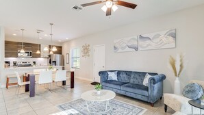A modern living room with a blue sofa, white coffee table, and a dining area with white chairs. - Golf, Dine & Unwind Poolside! Haines City Getaway (Haines City)