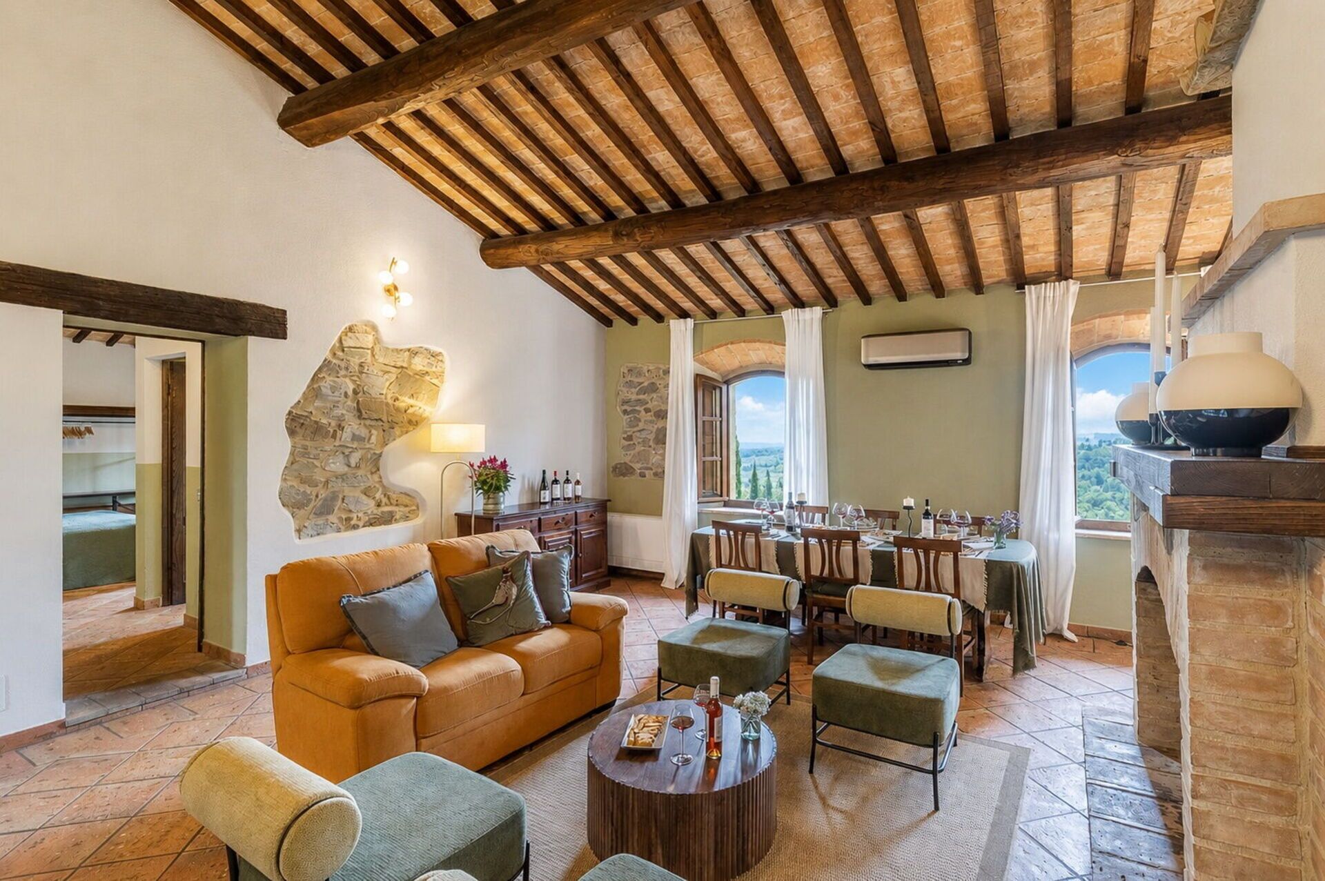 Un intérieur rustique avec un mur en pierre, des poutres en bois, un coin repas et une vue par la fenêtre.