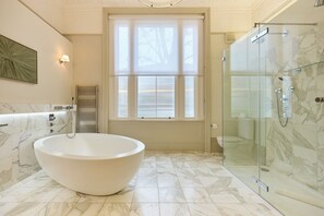 Et moderne badeværelse med et fristående badekar, en brusekabine med glasvægge og et stort vindue, der giver naturligt lys.