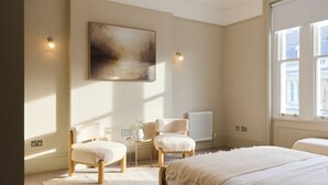 A bedroom with a large bed, two chairs, a small table, and a painting on the wall. - Kensington Five-Bedroom Townhouse (London)