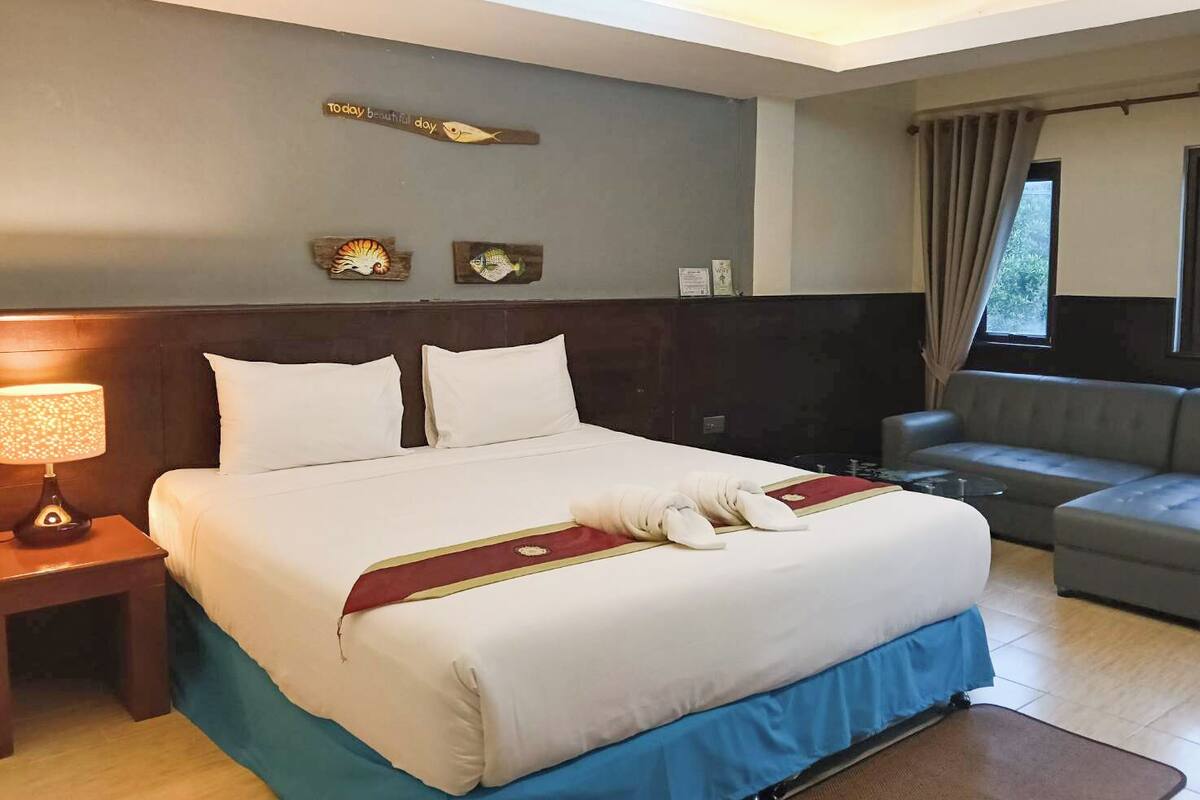 Une chambre d’hôtel avec un grand lit, une table de chevet avec une lampe, un canapé et des œuvres d’art décoratives au mur.