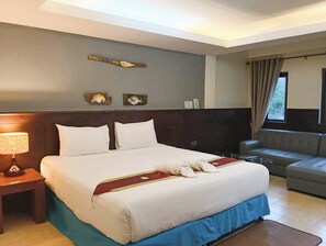 Quarto de hotel com cama grande, mesa de cabeceira com abajur, sofá e arte decorativa na parede.