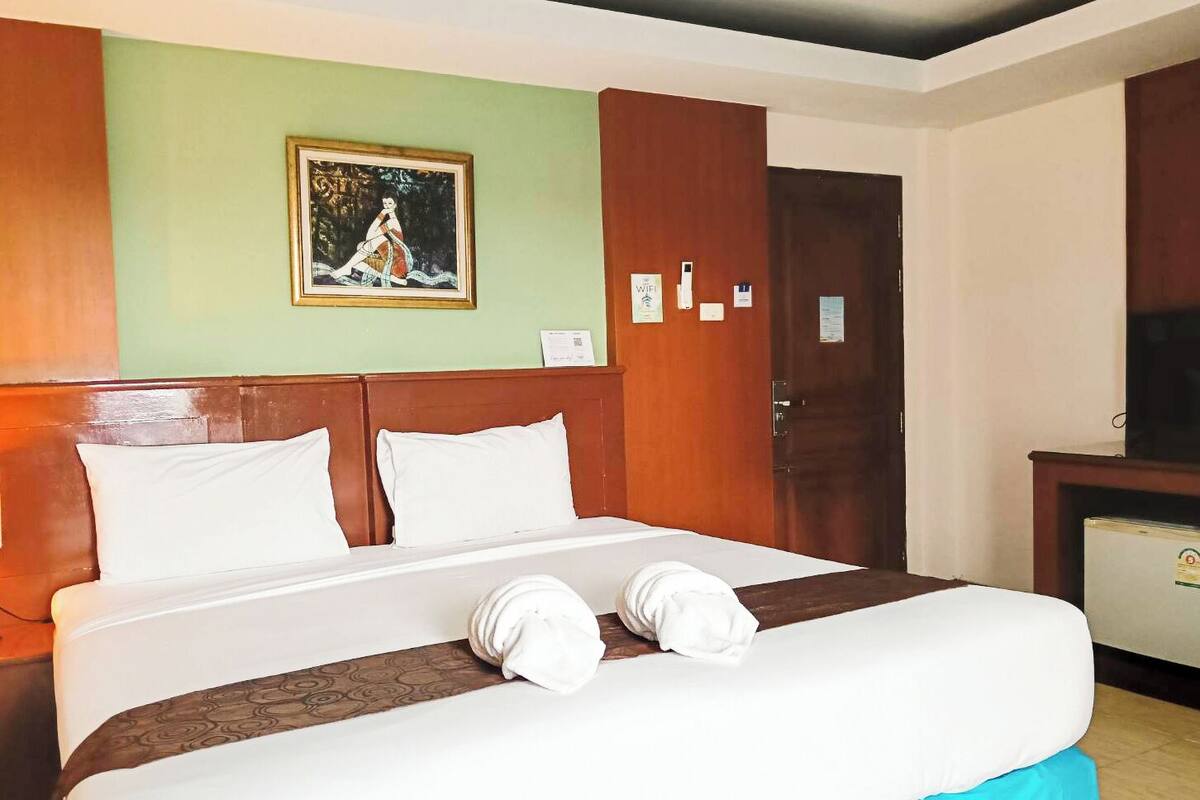 Une chambre d’hôtel avec un lit, une tête de lit en bois, un tableau au mur, un bureau avec une télévision et une porte.