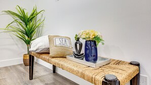 A woven bench with a white pillow labeled "SEA," a blue vase with flowers, and a woven basket. - Extended Stay in LA! Cozy Home 3 Mi to Downtown (Los Angeles)