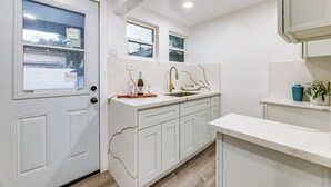 A kitchen with white cabinets, a sink, and a countertop. There is a window above the sink and a door on the left. - Extended Stay in LA! Cozy Home 3 Mi to Downtown (Los Angeles)