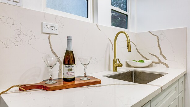 A kitchen with a marble countertop, a gold faucet, a wine bottle, and two wine glasses on a wooden board. - Extended Stay in LA! Cozy Home 3 Mi to Downtown (Los Angeles)