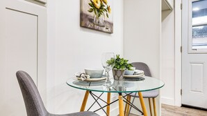 A dining area with a glass table, two chairs, a vase with flowers, and a painting on the wall. - Extended Stay in LA! Cozy Home 3 Mi to Downtown (Los Angeles)