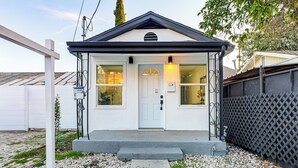 A small, single-story house with a white exterior, a dark roof, and a front door with a small porch. - Extended Stay in LA! Cozy Home 3 Mi to Downtown (Los Angeles)