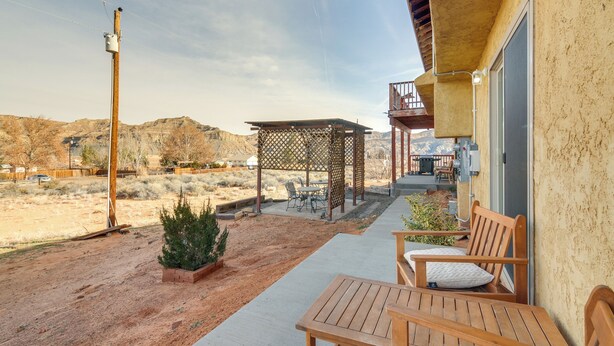 A patio with a wooden table and chairs, a covered seating area, and a view of a desert landscape. - Adventure Base 3 Near Lake Powell - Dog Friendly (Big Water)