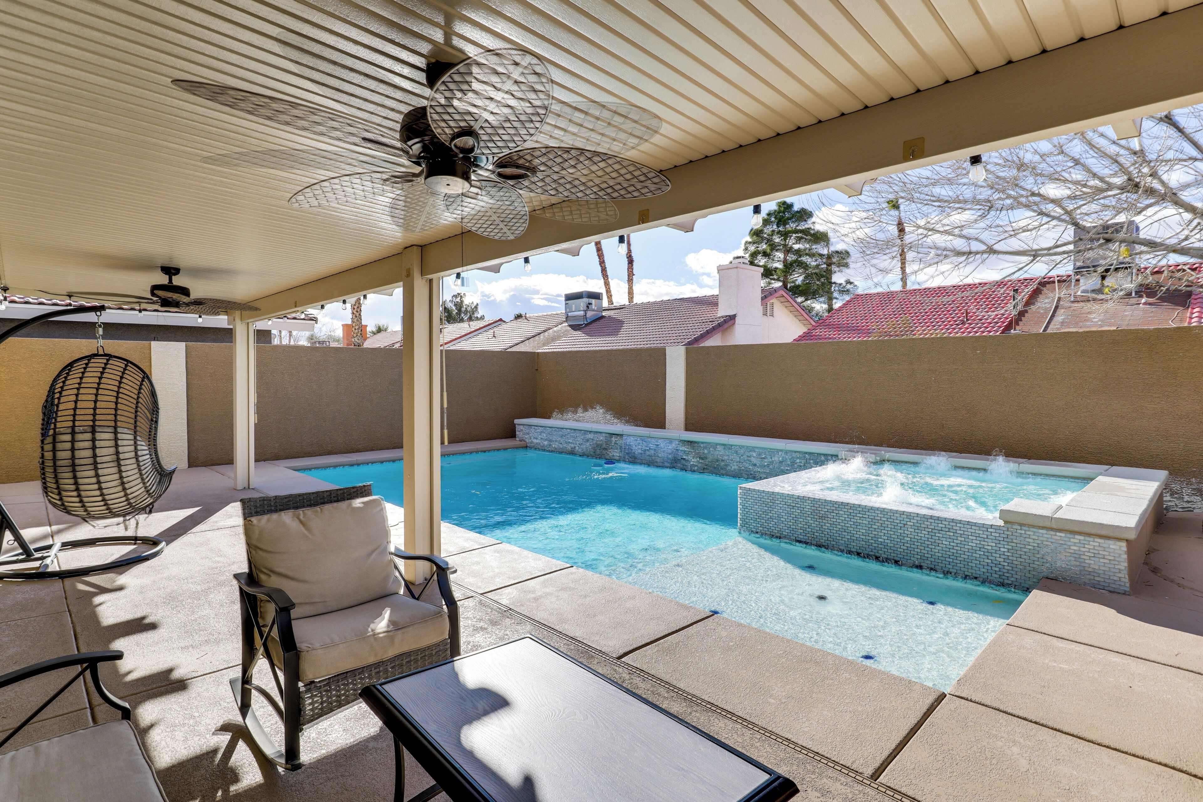 A covered outdoor swimming pool area with lounge chairs and a hot tub.