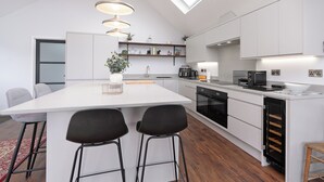 Et moderne køkken med en central ø, barstole, indbygget ovn og et ovenlysvindue.