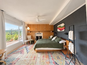 Une chambre avec un lit, une cheminée, une vue sur la verdure et une grande fenêtre.
