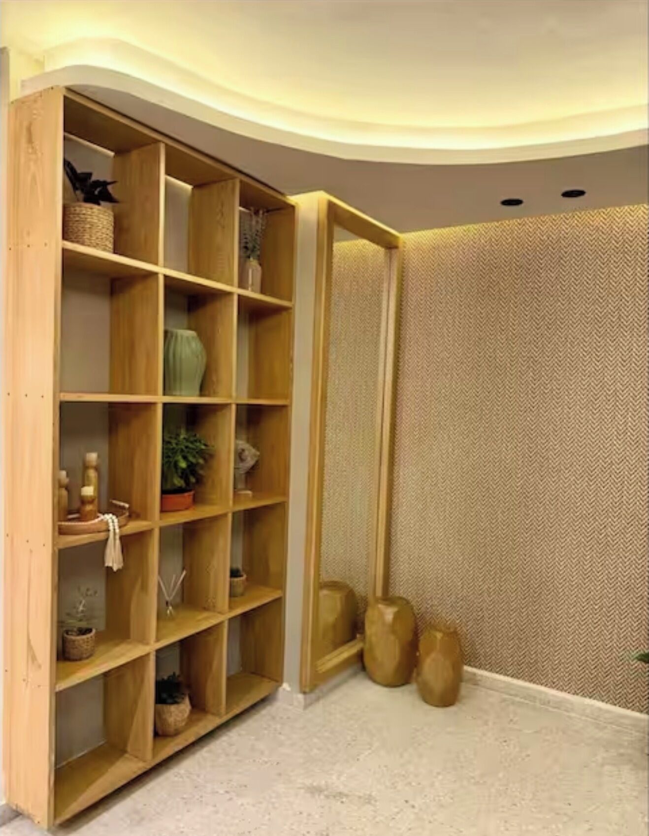 Una stanza angolare con un'unità di scaffalatura in legno contenente diversi oggetti decorativi e una parete strutturata.
