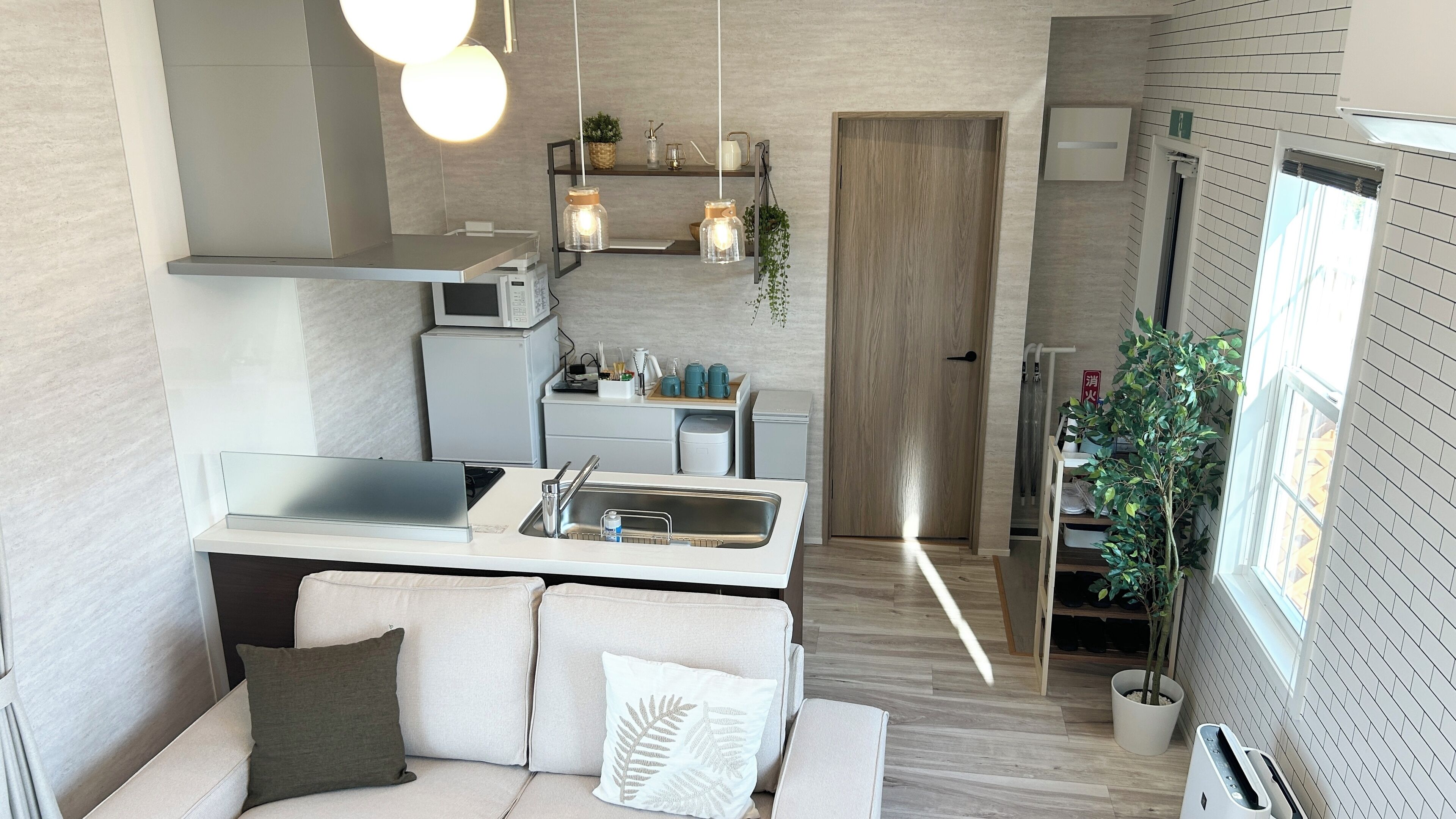 A compact kitchen with a central island, a microwave, and a sink. There is a sofa with a fern pillow and a potted plant by the window.