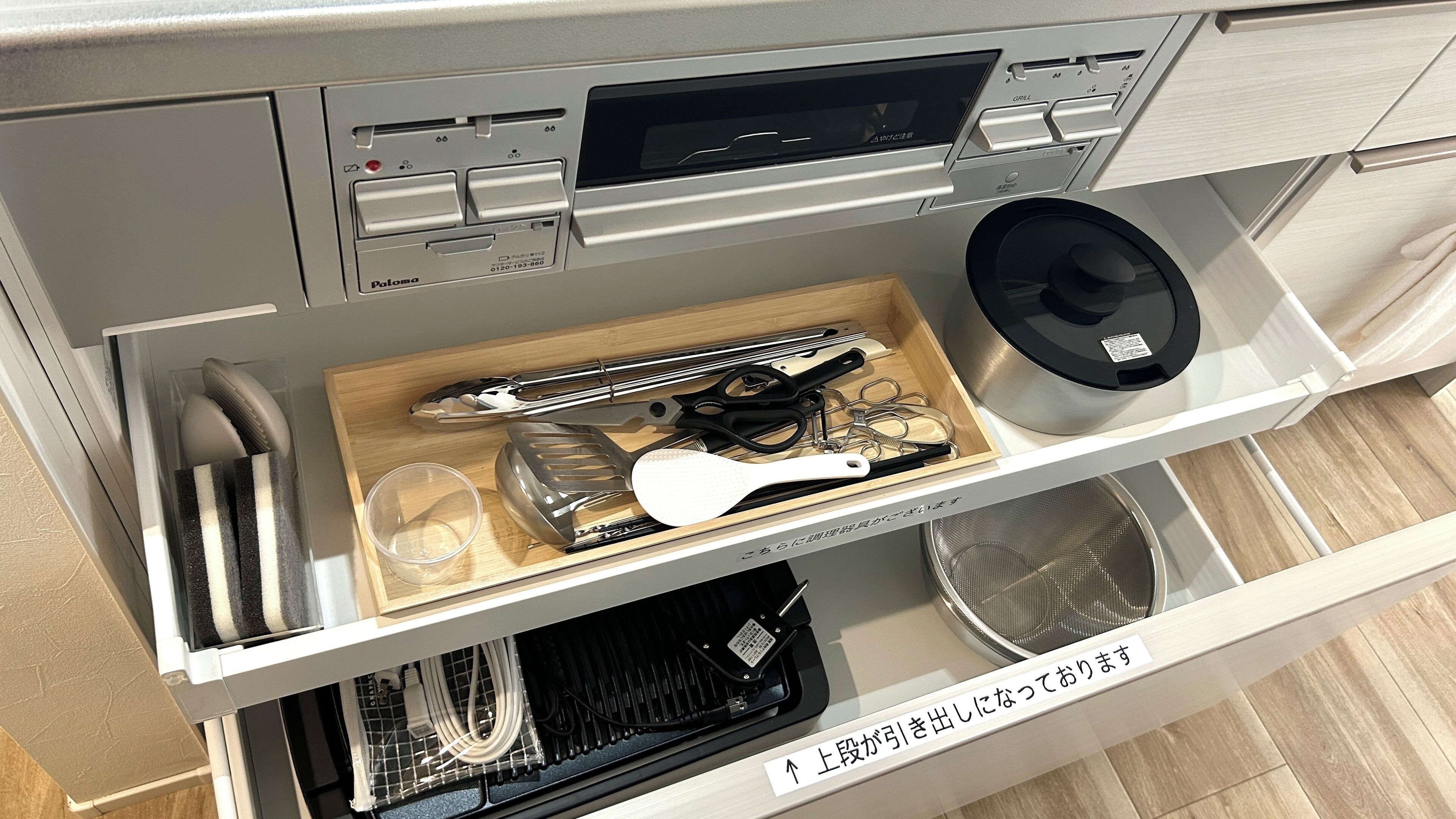 A kitchen drawer with utensils, a spatula, and a rice cooker.
