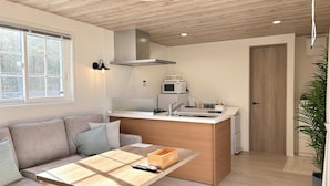 Un espacio habitable pequeño con kitchenette, un sofá, una mesa de centro y una planta en maceta.