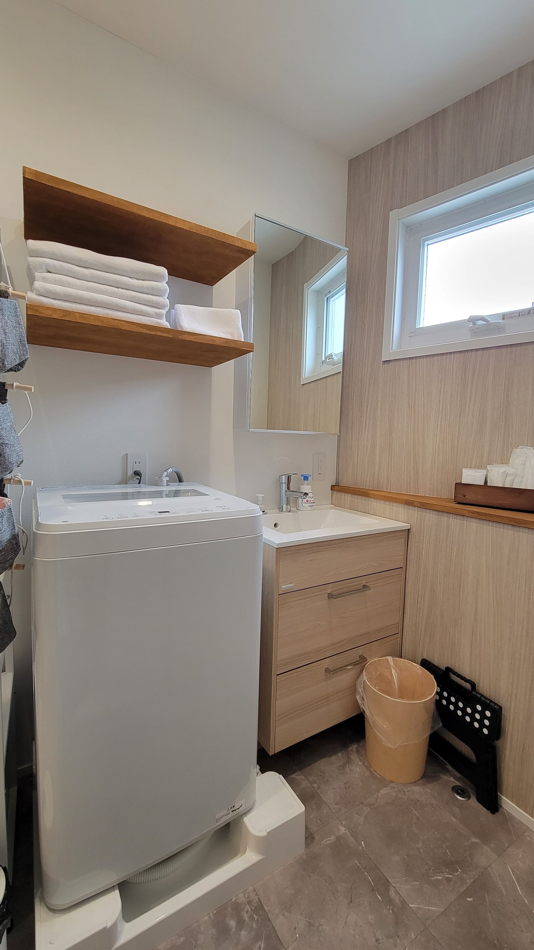 A modern bathroom with a built-in washing machine, a sink, a mirror, and wooden shelving.