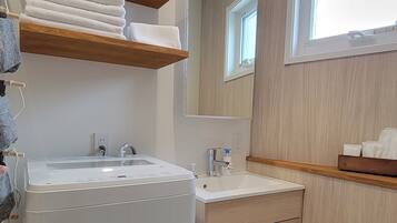 A modern bathroom with a built-in washing machine, a sink, a mirror, and wooden shelving.