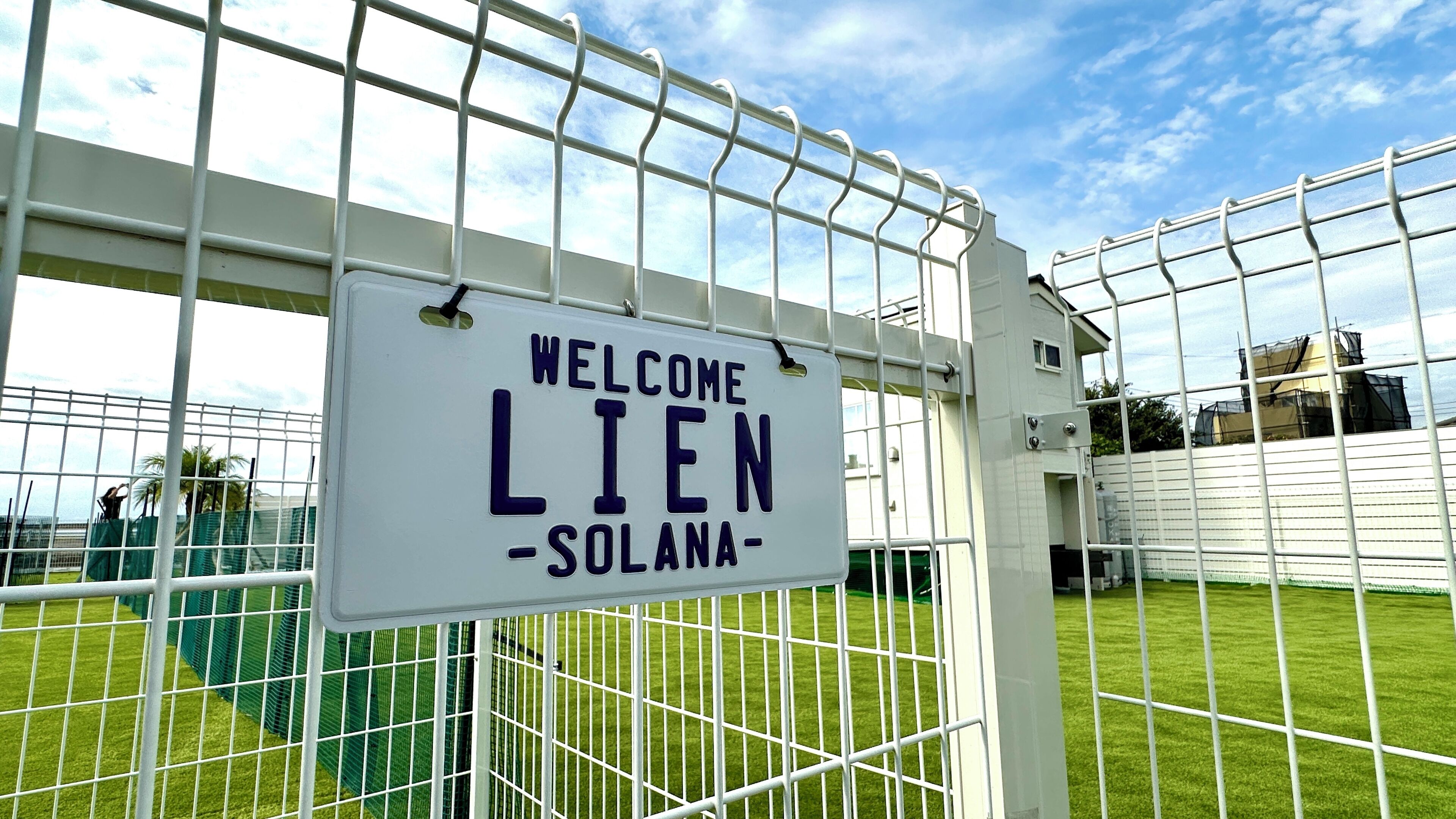 A welcome sign at the entrance of a facility with a metal fence and green grass.