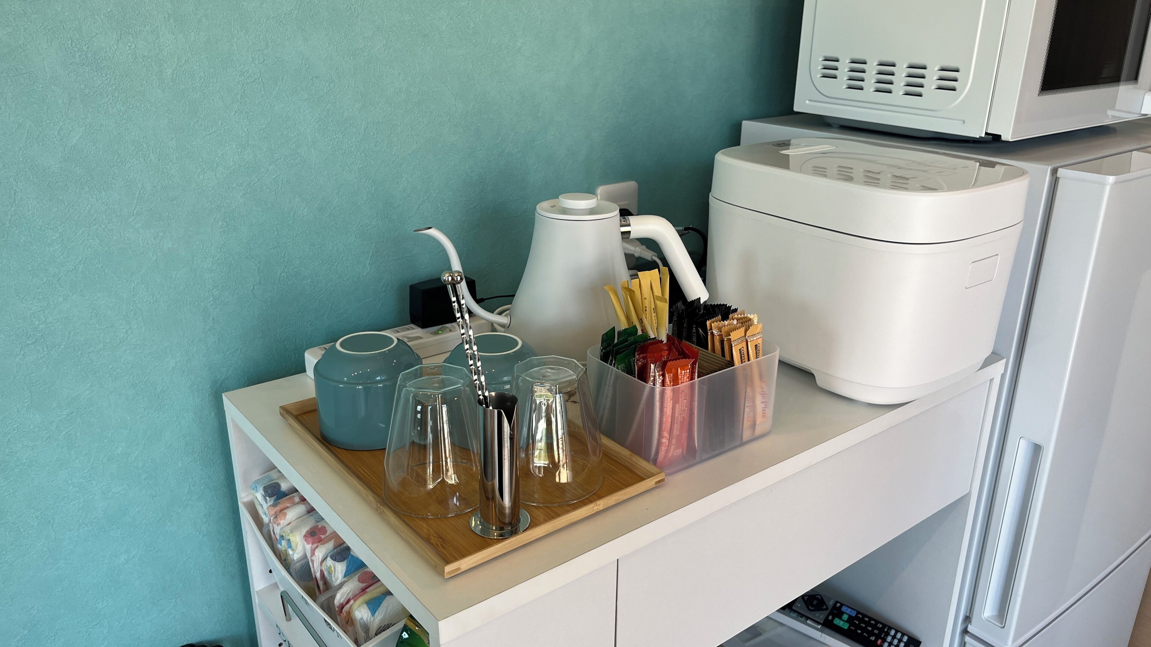 Een aanrecht met een magnetron, een rijstkoker en een koffiezetapparaat. Ook staan er glazen, een waterkoker en een bak met bestek.