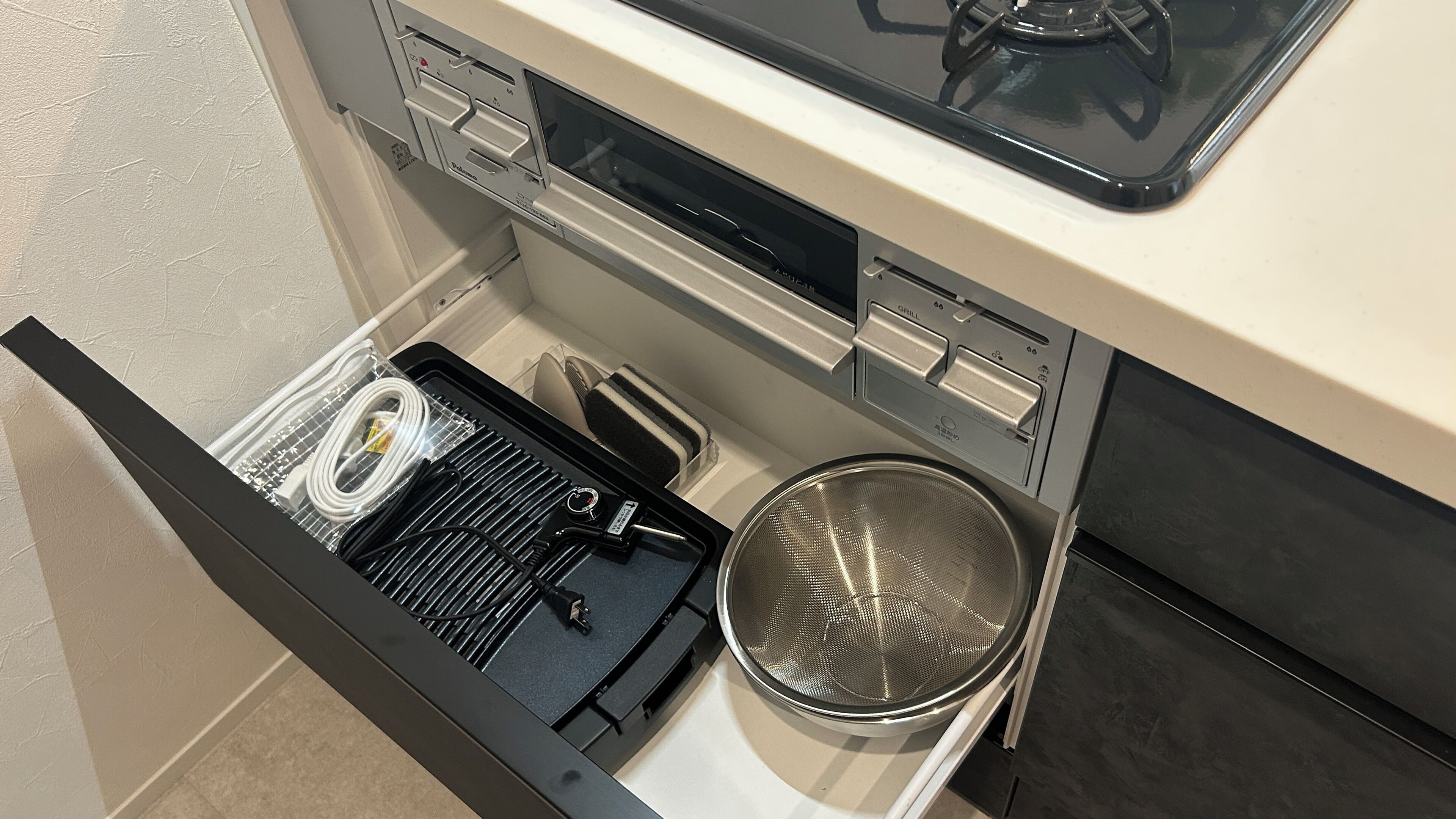 Una cocina con horno empotrado, parilla y un colador de acero inoxidable.