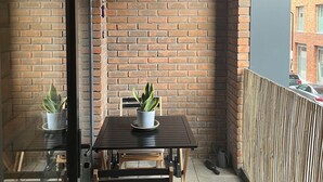 Un balcone angolare con un muro in mattoni, un tavolo di legno con due piante in vaso e una panca imbottita.