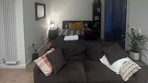 Un accogliente soggiorno con un divano grande, un letto con copriletto a quadretti, un termosifone, uno specchio e una pianta in vaso.