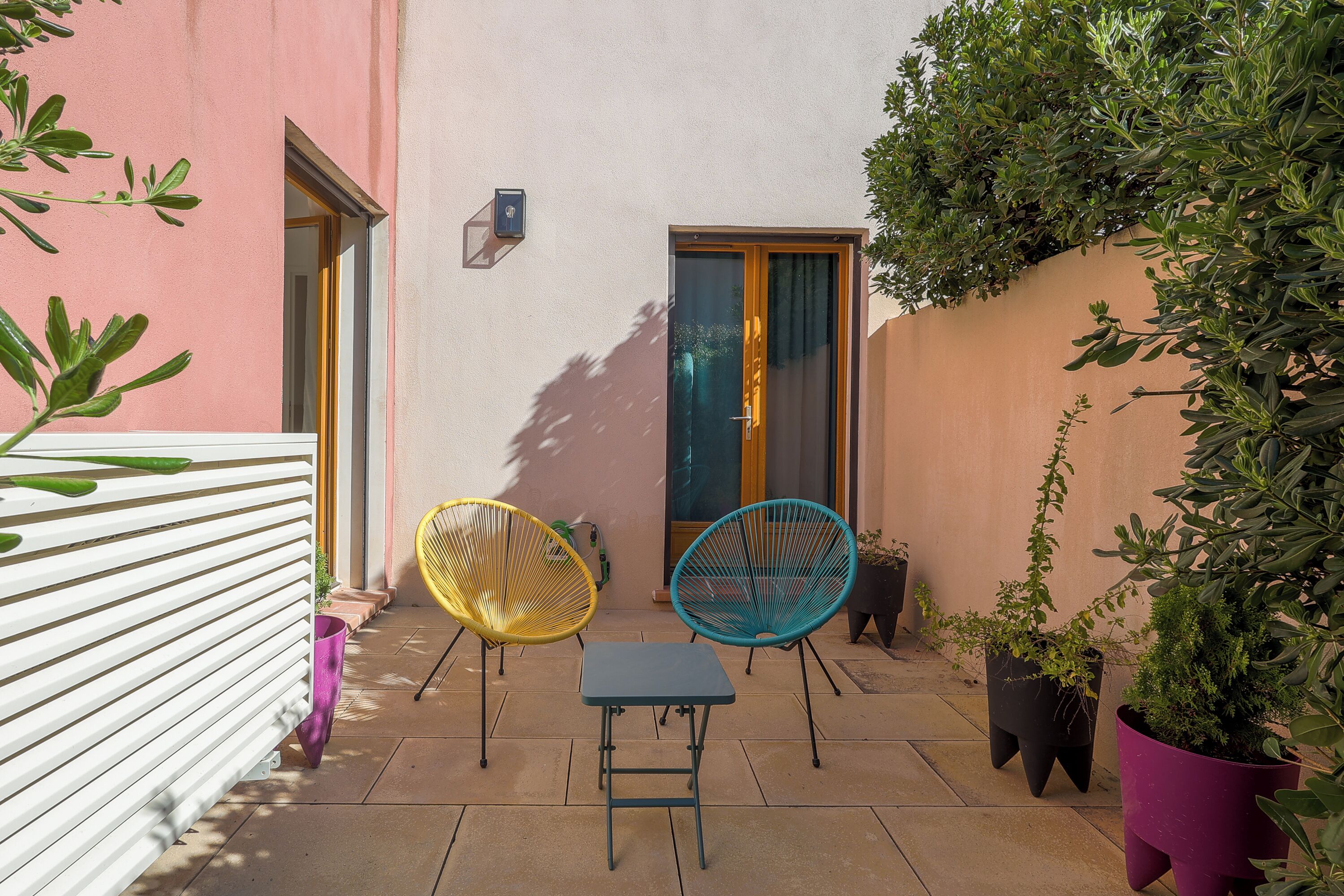 A patio with two chairs and a table, a door, and potted plants.