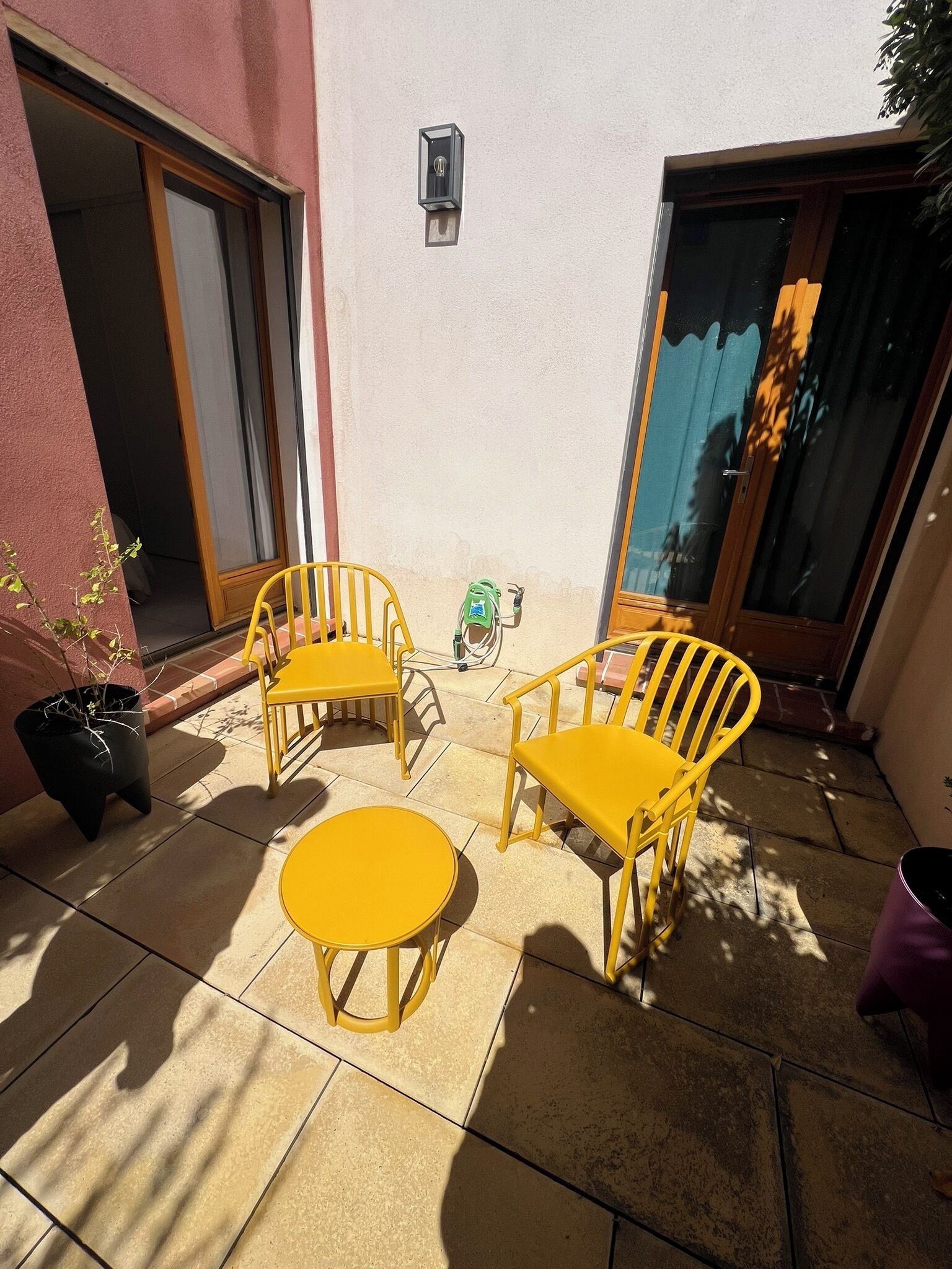 A patio with yellow chairs and a small round table, a potted plant, and a bicycle.