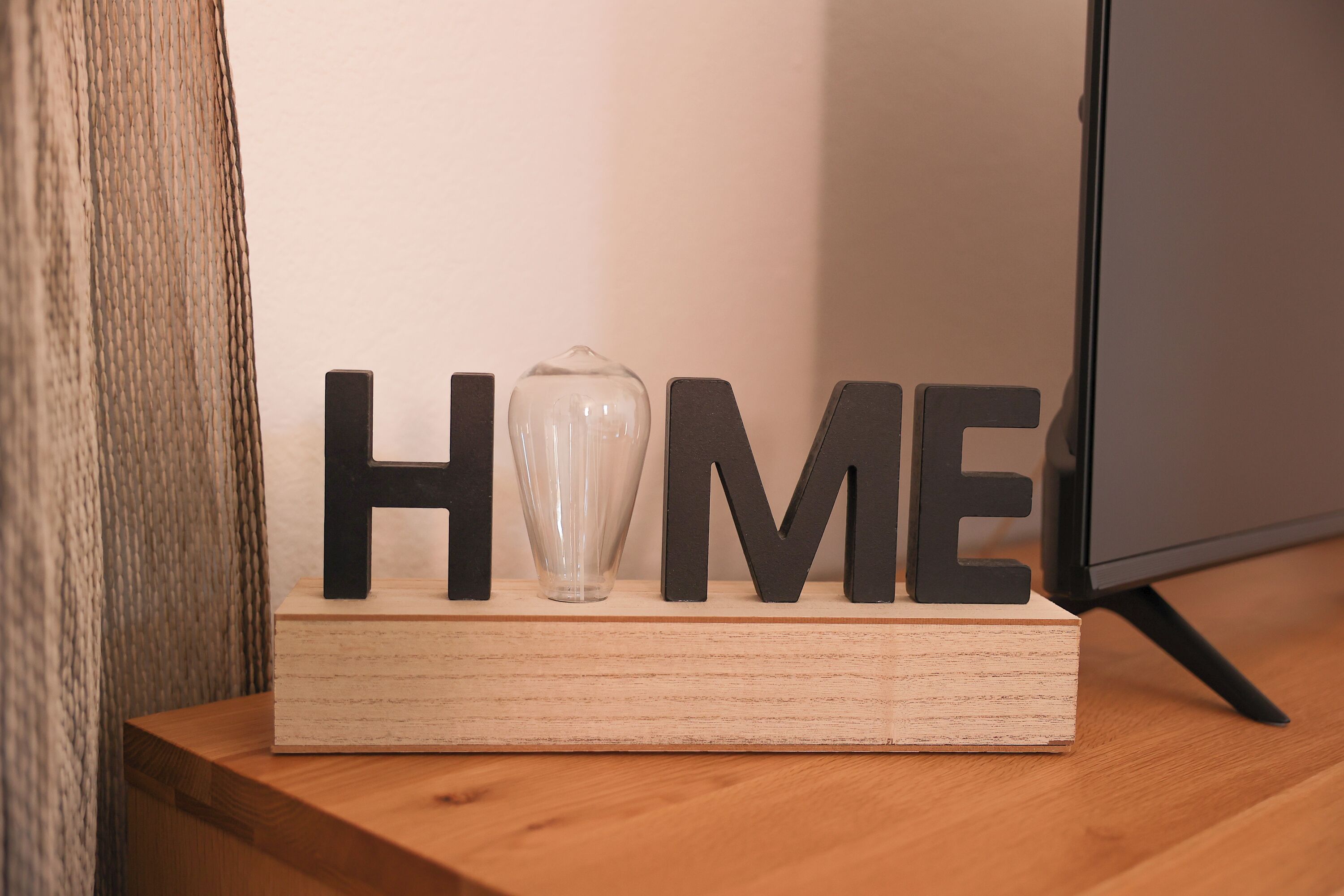 Een houten blok met de letters 'HOME' en een glazen vaas erboven.